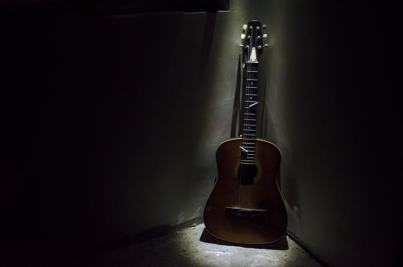 Acoustic guitar leaning on rusty wall in dark room with lights