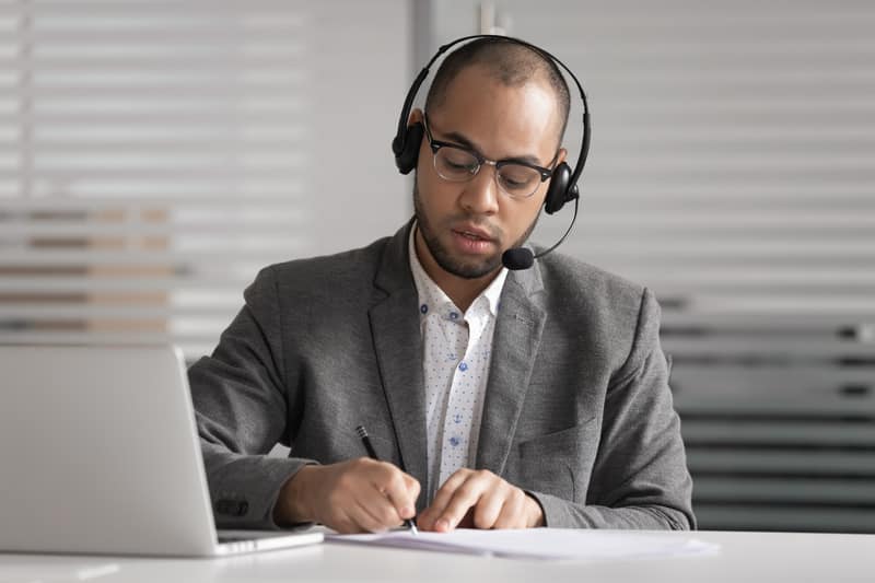African customer support agent wear headset write notes make videocall