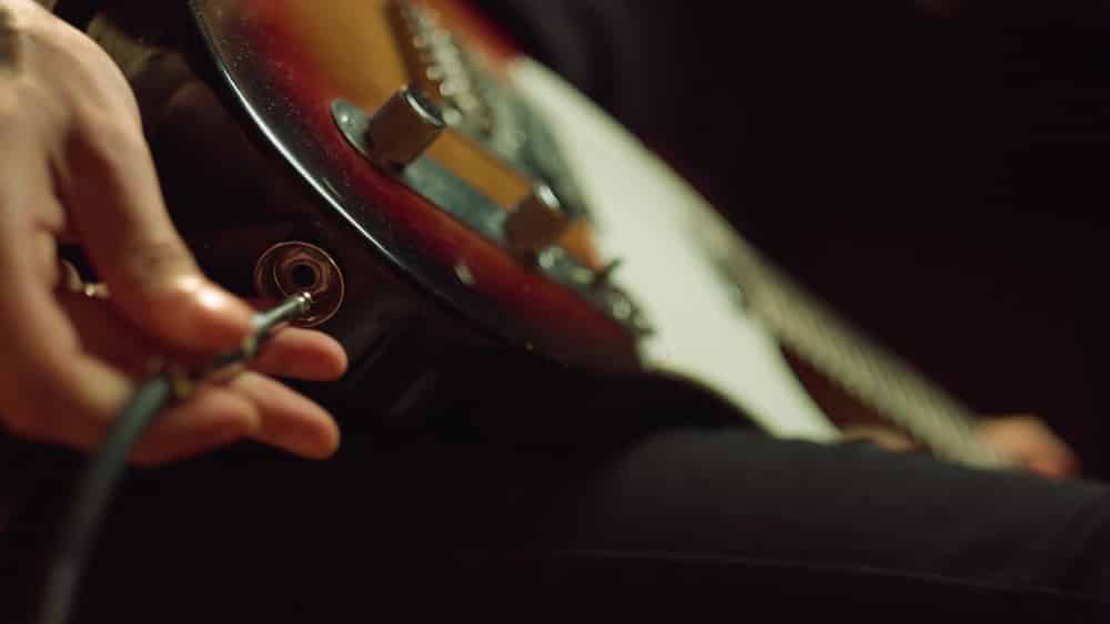 Closeup man hand sticking plug to guitar