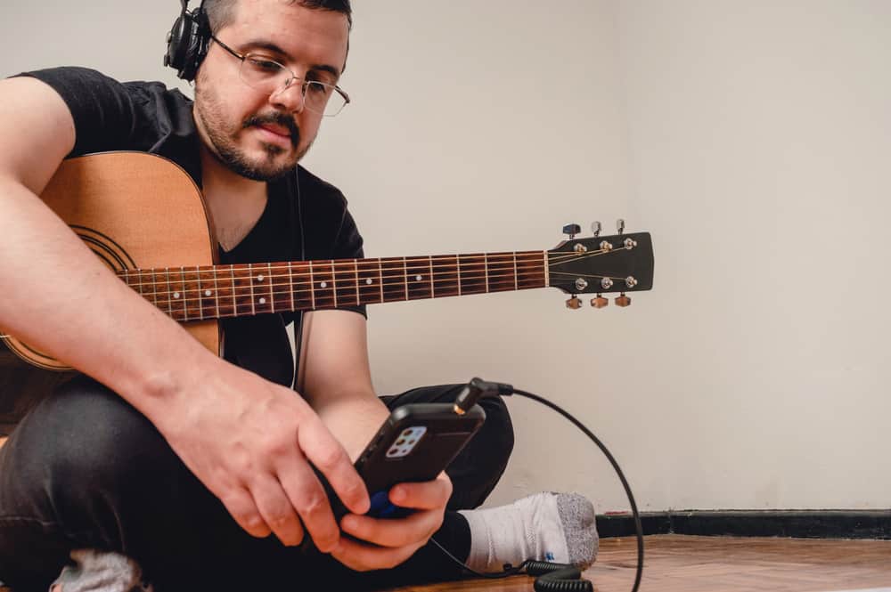 Man sitting in the floor with his guitar checking the phone 