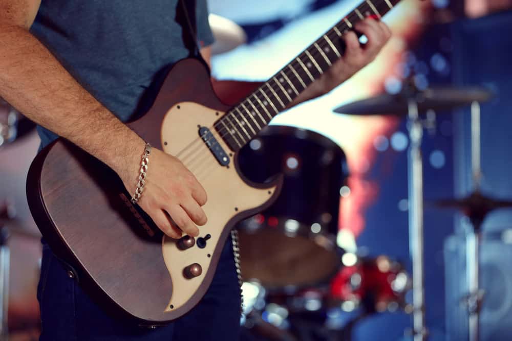 Young man playing on electric guitar close up