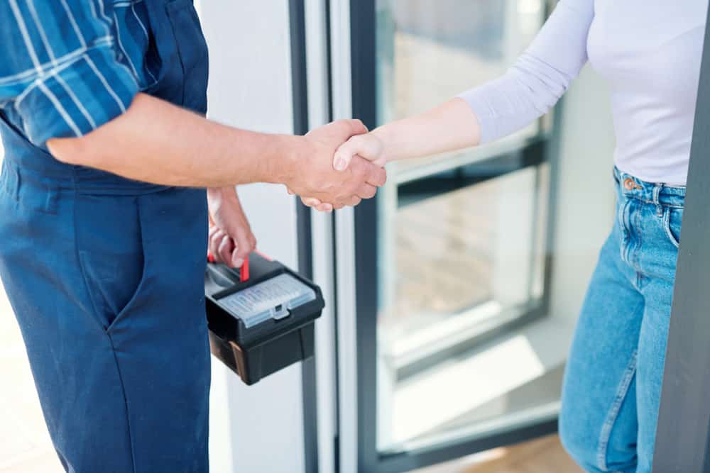 Young woman and technician saying goodbye while shaking hands after repair work