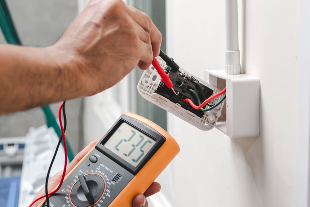 Electrician is using a digital meter to measure the voltage at the power outlet