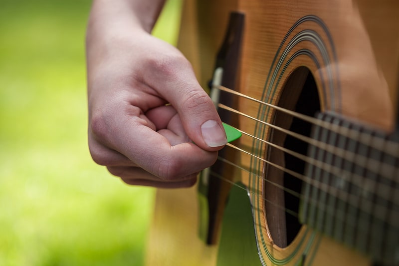 Musician playing guitar using pick color green