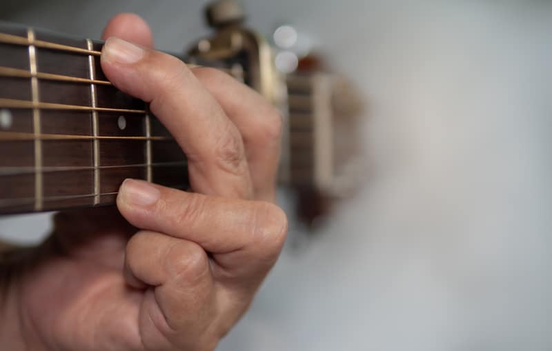 Hand holds the neck of classic wooden guitar play G chord with capo