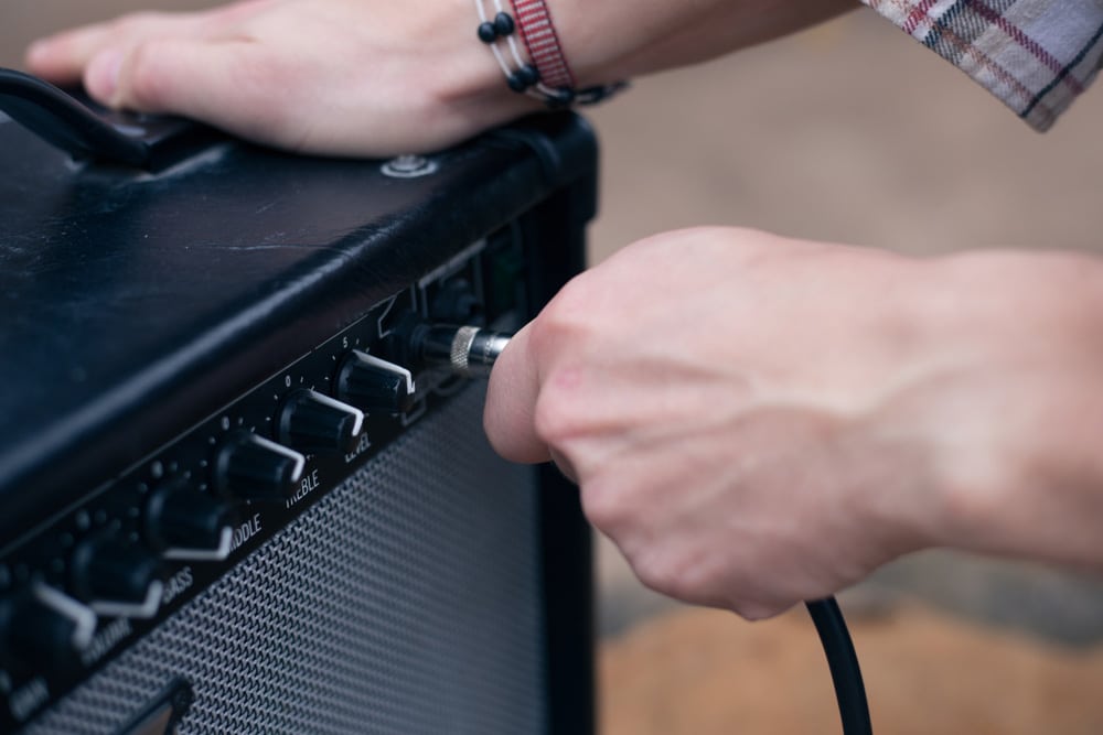 Hand inserts a cord jack into a combo amplifier for electric guitar