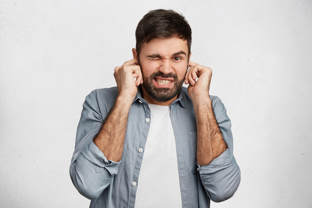 Male plugs ears with displeased expression 