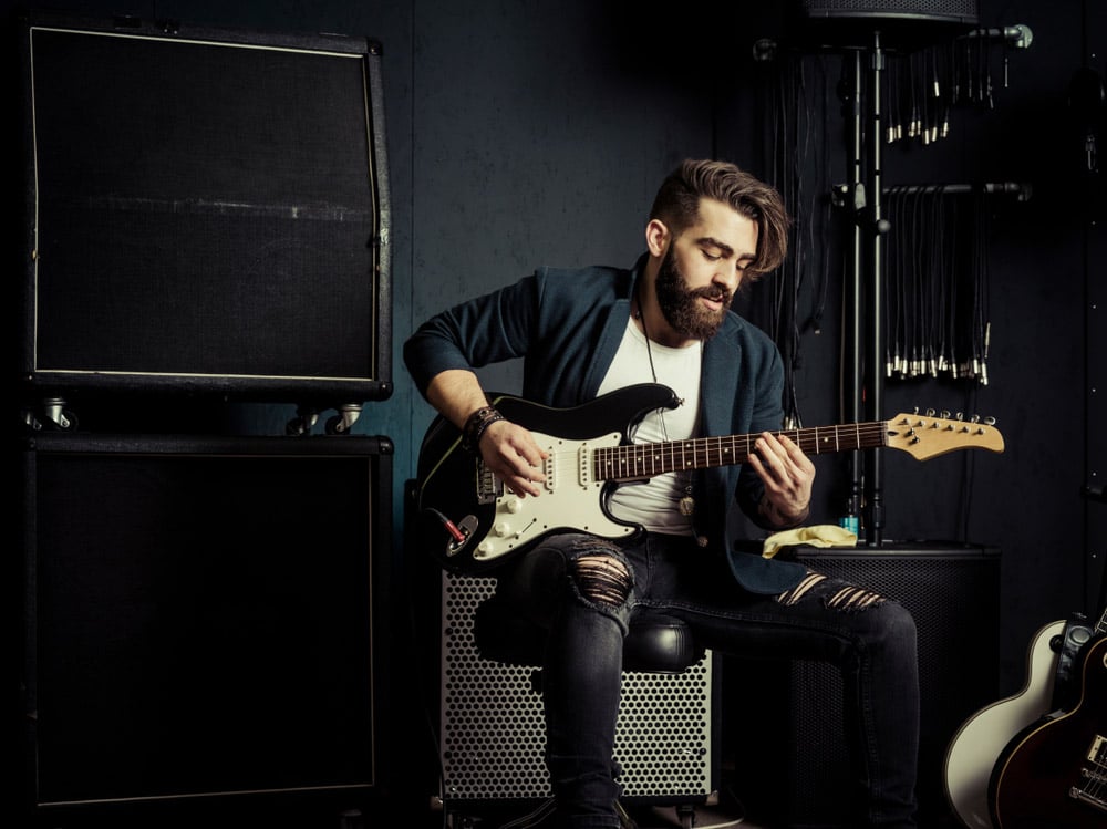 Man with beard sitting and playing his electric guitar