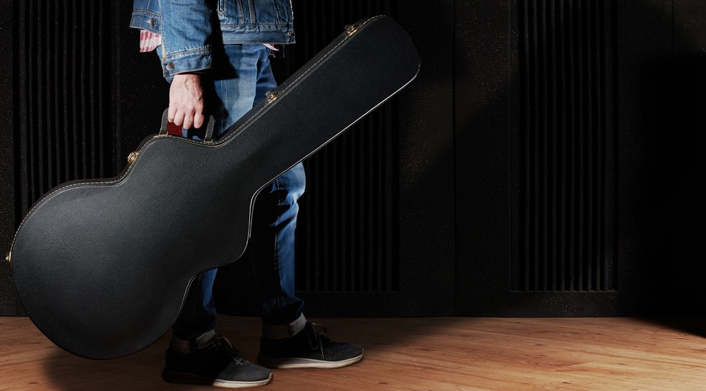 Man dressed in jeans holding guitar case 