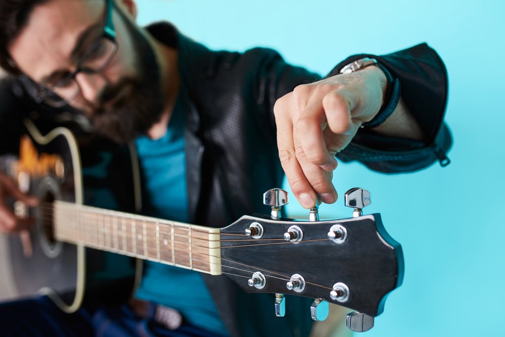 Bearded hipster man hand adjusting acoustic guitar