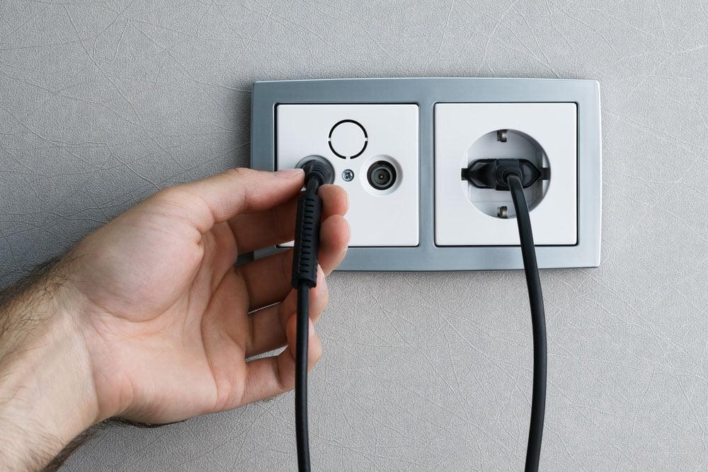 A man hand plugging antenna cable to the TV outlet