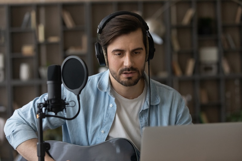 Close up man in headphones playing guitar using laptop