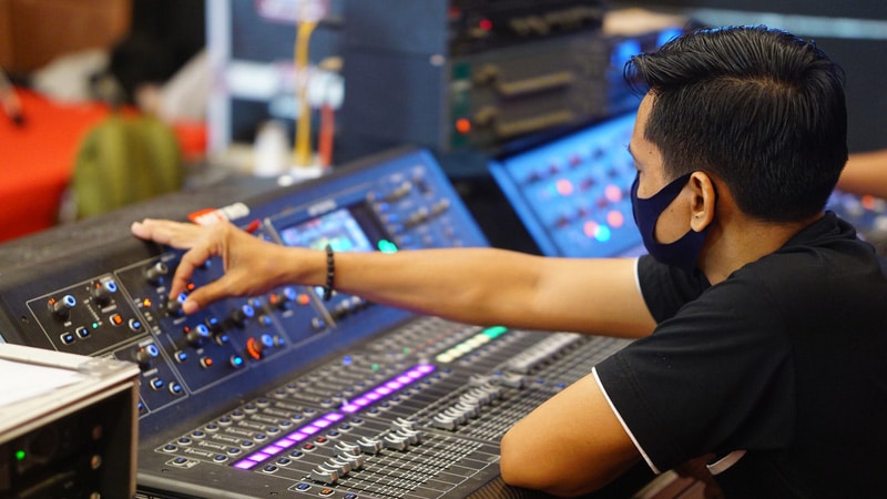 A man in a mask is turning an audio mixer knob