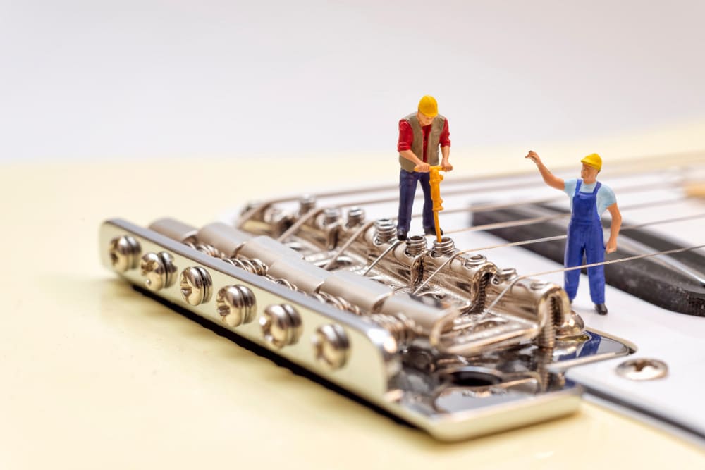 Miniature workers adjusting the bridge of an electric guitar