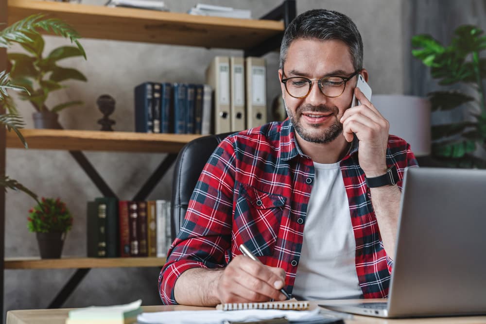 Smiling man writing notes while making phone call